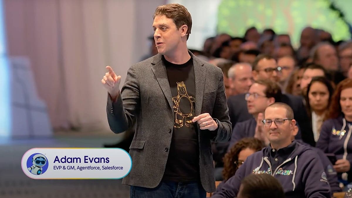 Adam Evans, EVP & GM of Agentforce at Salesforce, speaking at the Salesforce TrailblazerDX (TDX) 2025 conference. He is addressing an engaged audience while wearing a blazer over a black t-shirt featuring a gold Agentforce mascot. The event, held at Moscone Center in San Francisco, highlights AI-driven automation and digital labor innovations within the Salesforce ecosystem